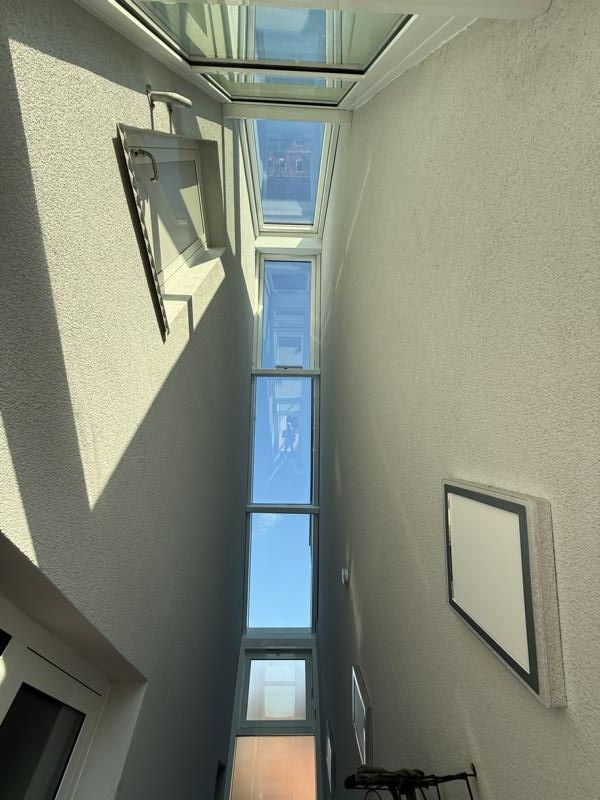 Innenansicht eines schmalen Treppenhauses mit Oberlichtern und blauem Himmel darüber.