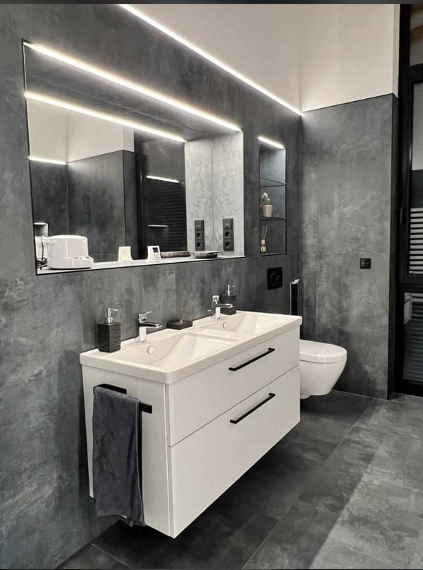 Modernes graues Badezimmer mit schwebendem Waschtisch, großem Spiegel, Wandleuchten und Toilette.