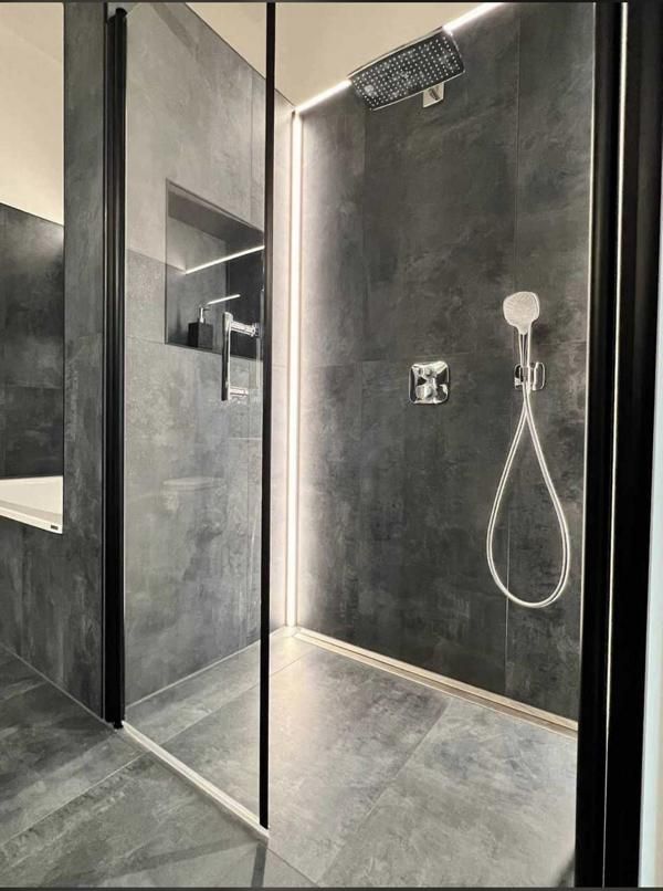 Moderne, schwarz geflieste Dusche mit Glasabtrennung, wandmontierten Armaturen und Handbrause