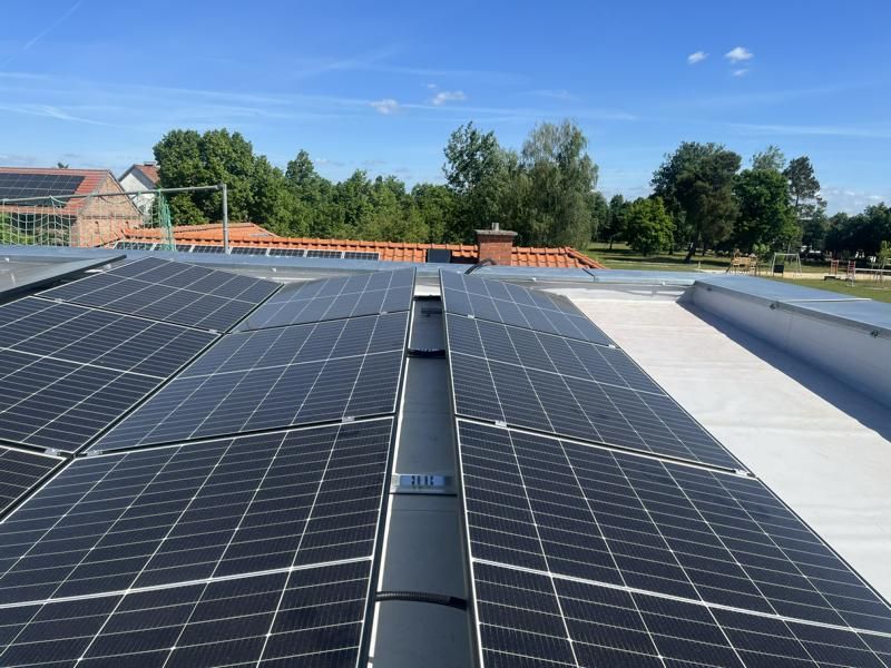 Solarpaneele auf einem Dach unter klarem, blauem Himmel, im Hintergrund Bäume und Häuser.