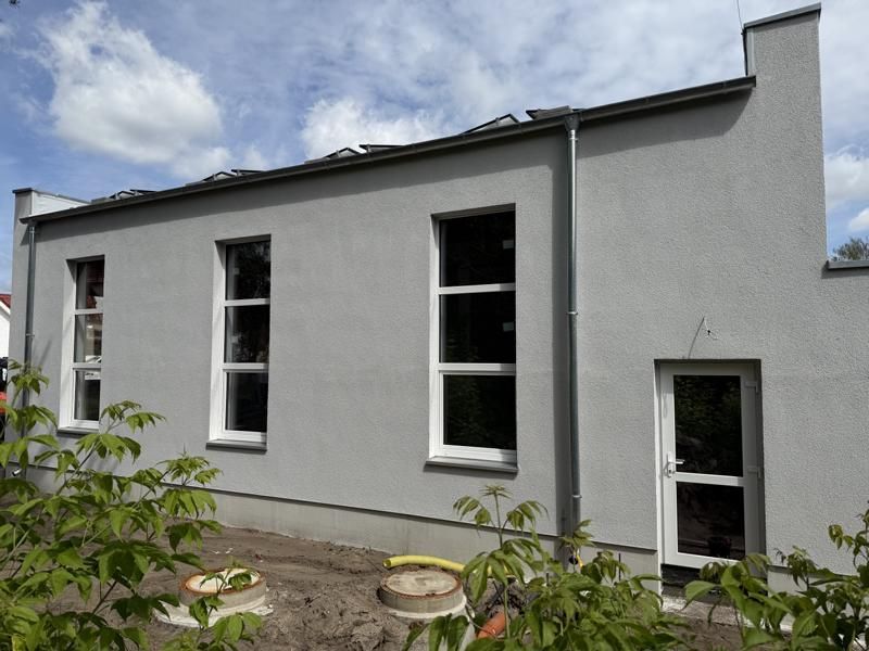 Außenansicht eines weißen Hauses mit zwei hohen Fenstern und einer kleinen Seitentür unter einem bewölkten Himmel