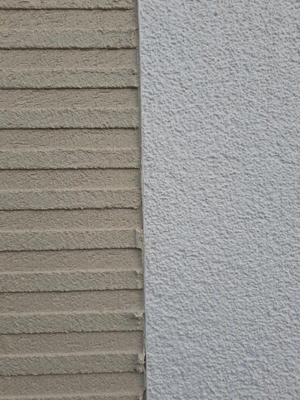 Nahaufnahme einer strukturierten, beige-grauen Außenwand mit horizontaler Verkleidung neben Stuck.