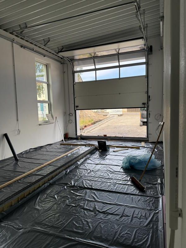 Teilweise ausgebauter Garageninnenraum mit isolierten Wänden, offenem Rolltor und kunststoffbedecktem Boden.