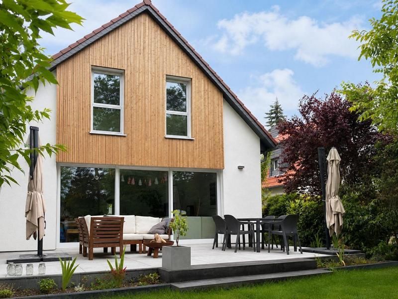 Modernes zweistöckiges Haus mit Holzverkleidung, Terrasse, Essbereich im Freien und Sonnenschirm in einem grünen Garten