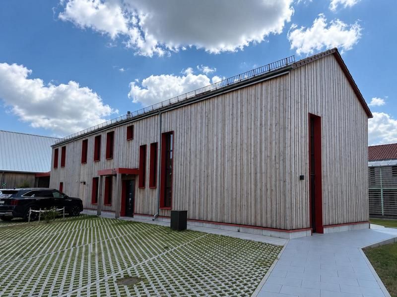 Modernes zweistöckiges Holzgebäude mit roten Verzierungen und einem gepflasterten Innenhof unter blauem Himmel