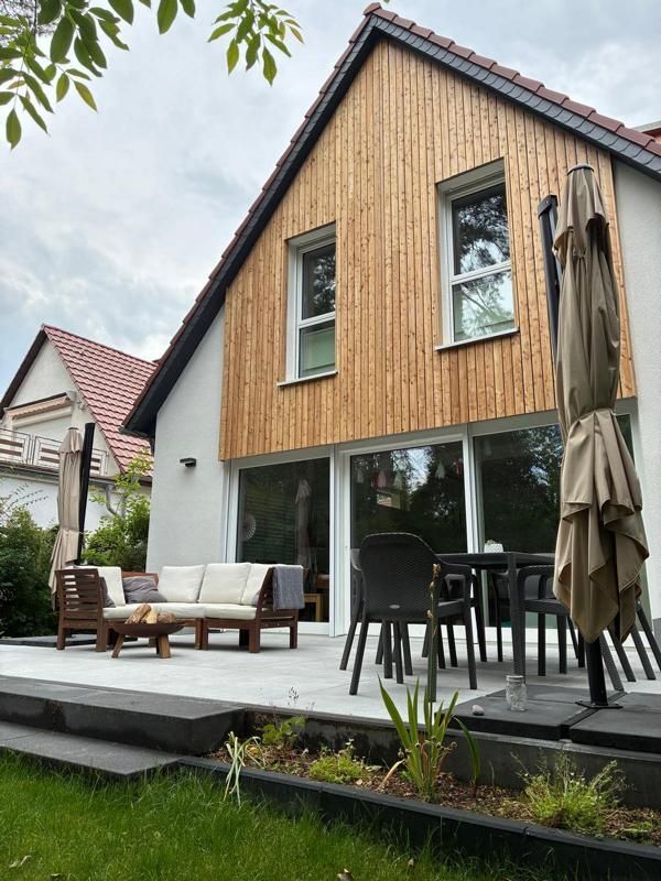 Modernes Holzhaus mit Terrasse, Sitzgelegenheiten im Freien und geschlossenem Sonnenschirm an einem kleinen Garten