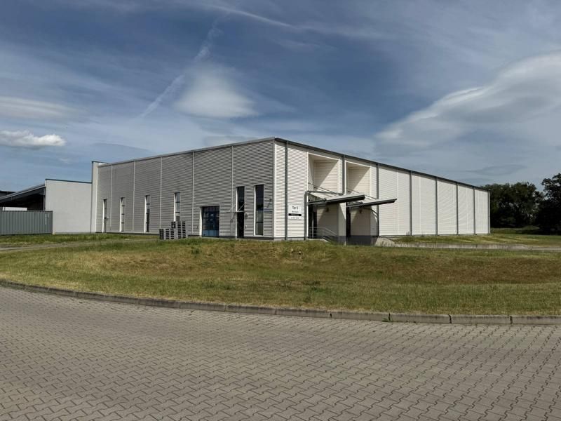 Große, weiße Industriehalle mit gepflasterter Zufahrt und Rasenfläche unter blauem Himmel