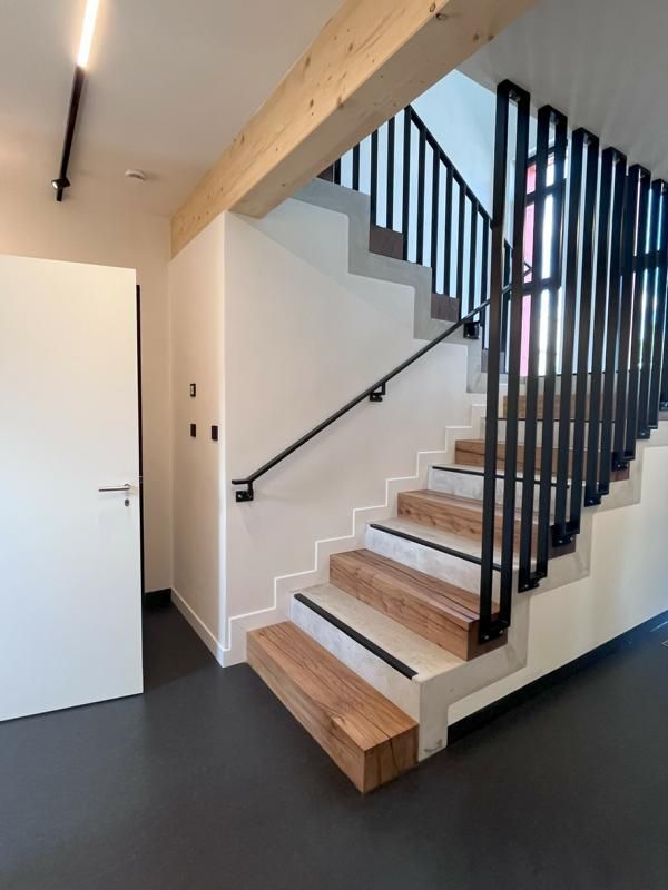 Moderne Innentreppe mit Holzstufen, schwarzem Geländer und weißen Wänden in einem minimalistischen Flur