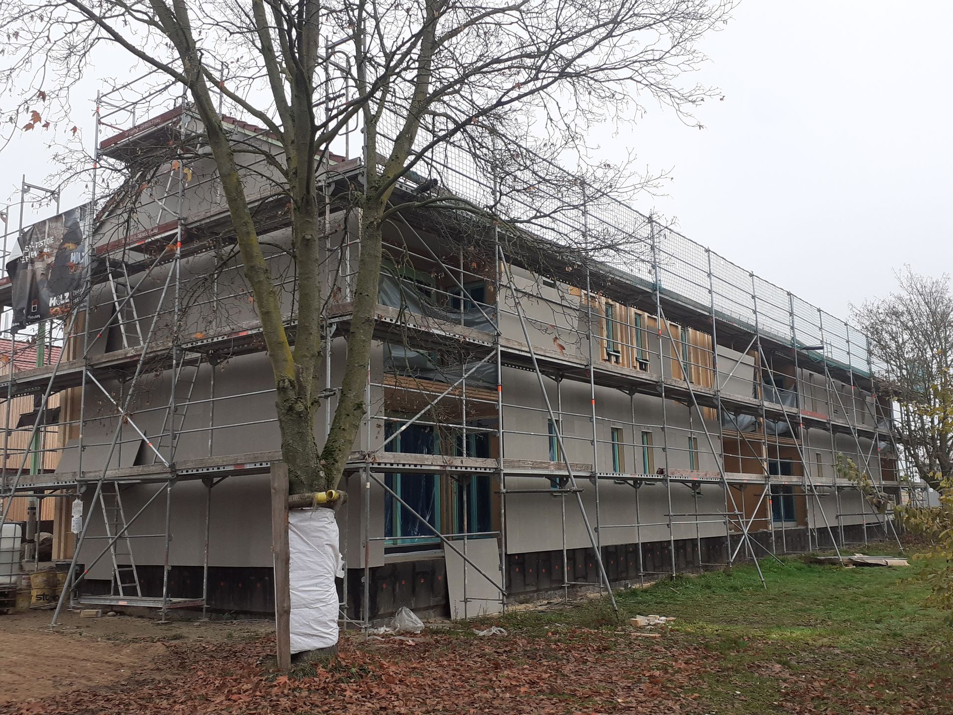 Gebäude wird renoviert, Gerüst vorhanden, Baum davor, bewölkter Tag.