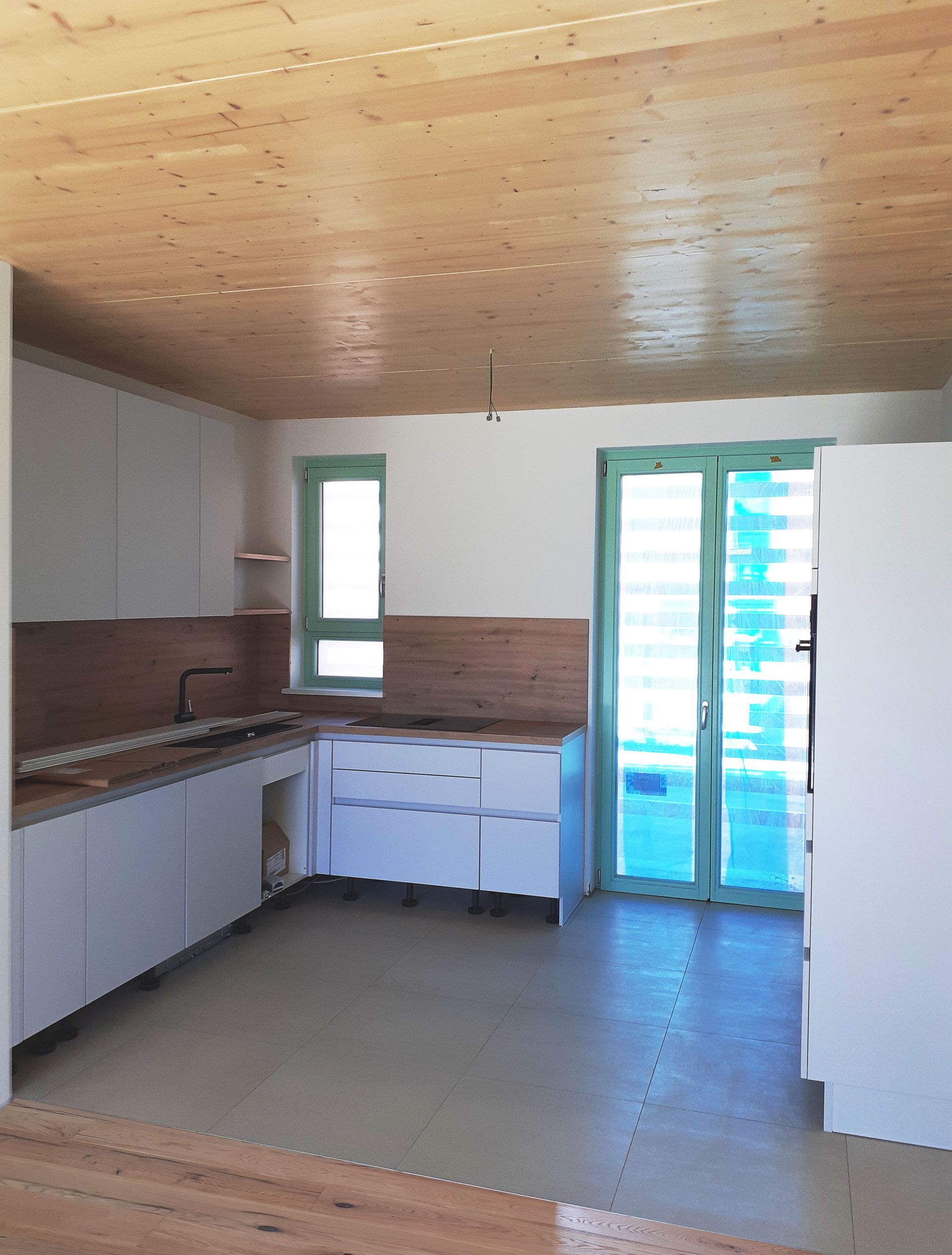 Moderne Küche mit heller Holzdecke, weißen Schränken und türkisfarbenen Fenster- und Türrahmen.