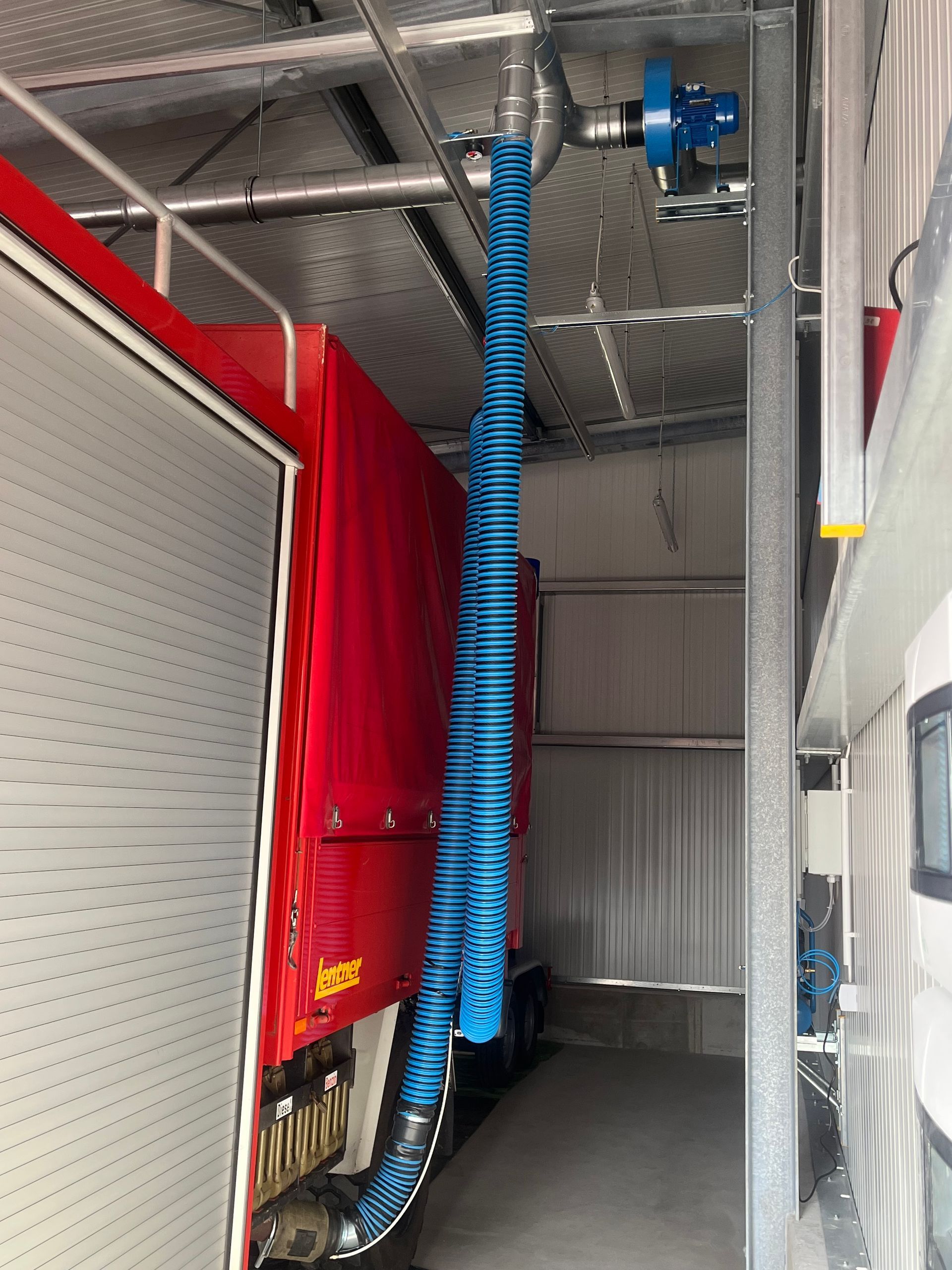 Innenraum eines LKW-Anhängers mit roter Ladung, einem blauen Belüftungsschlauch und Metallregalen.