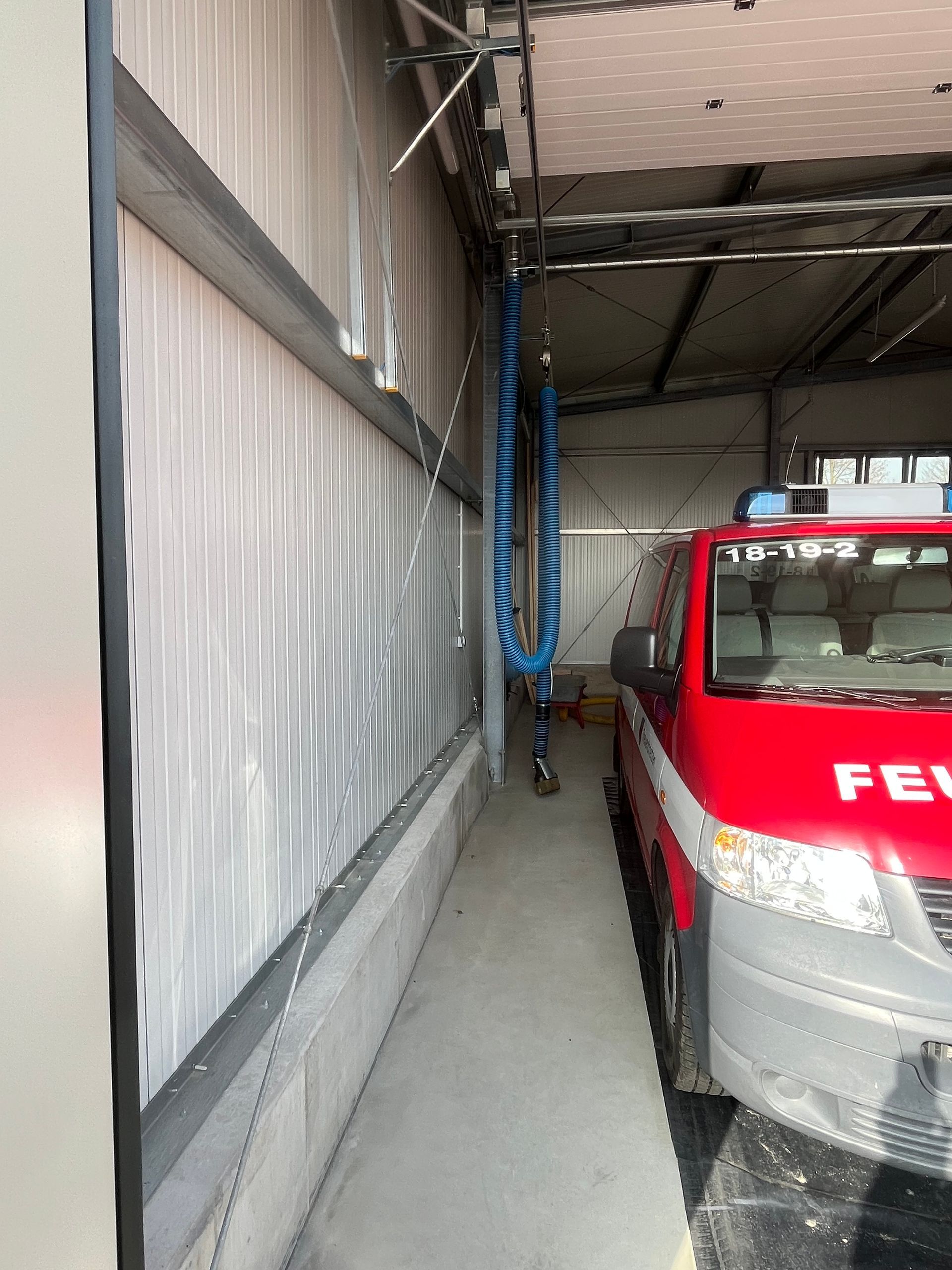 Ein roter FEDEX-LKW parkt in einer schmalen Garagenbucht neben einer Vorhangfassade und einem herabhängenden Schlauch.