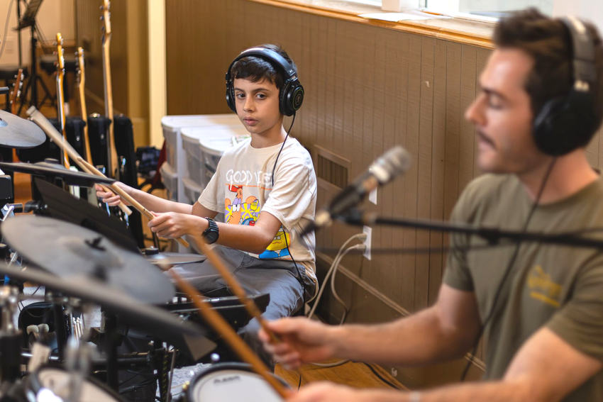A boy and his teacher play drums together during a private lesson.