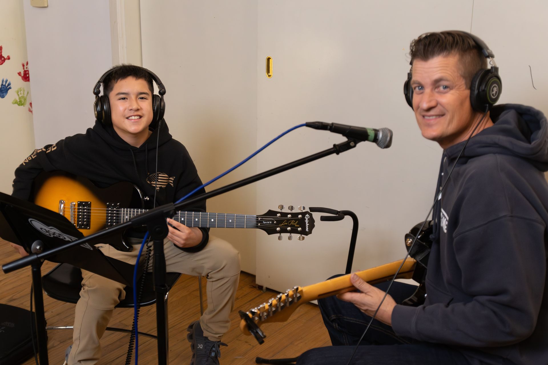 A boy and his music teacher smile wearing headphones and about to play guitars in a recording studio.