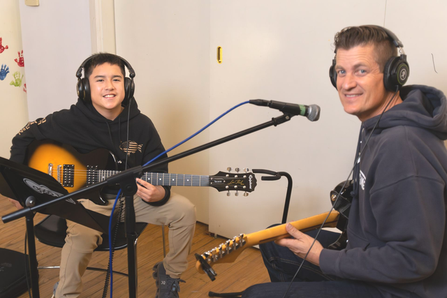 A boy and his teacher play guitar during an electric guitar music lesson.