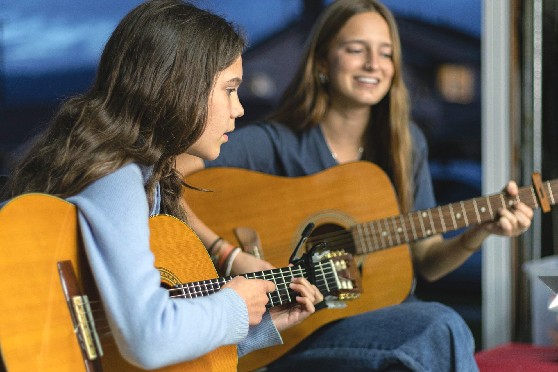 A girl and her music teacher holding acoustic guitars.