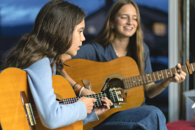 A girl and her teacher play guitar during a private music lesson.