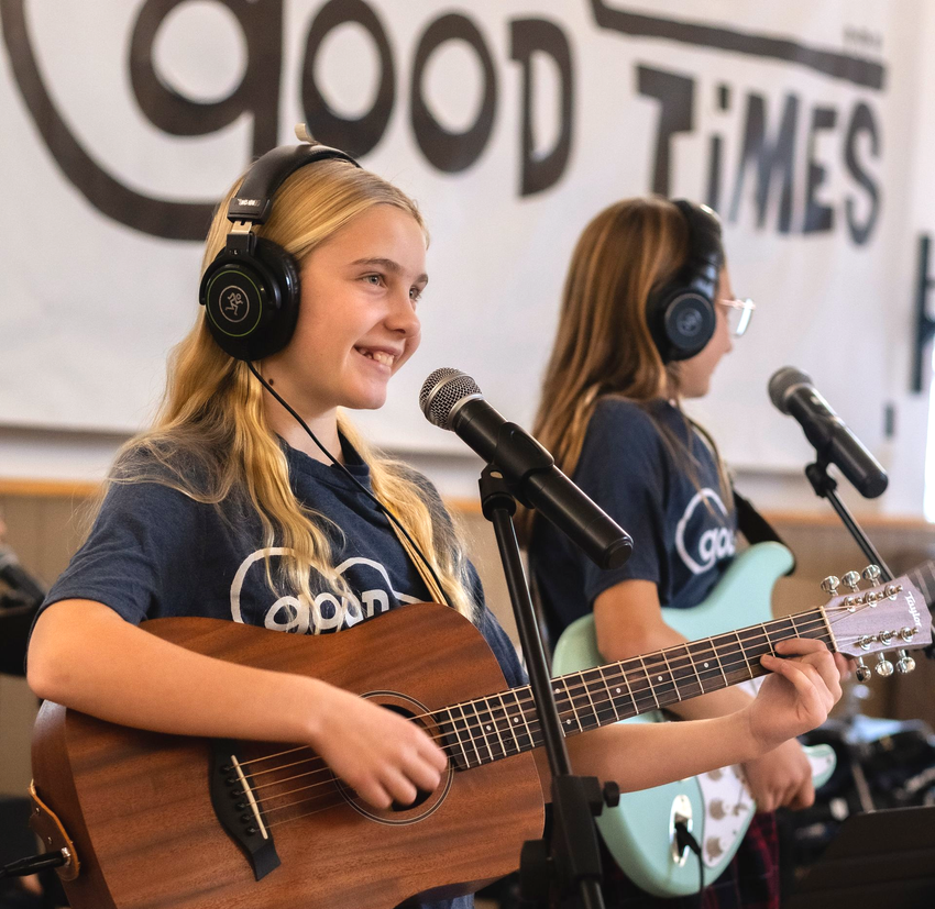 Girls smiling in front of microphones during band practice.
