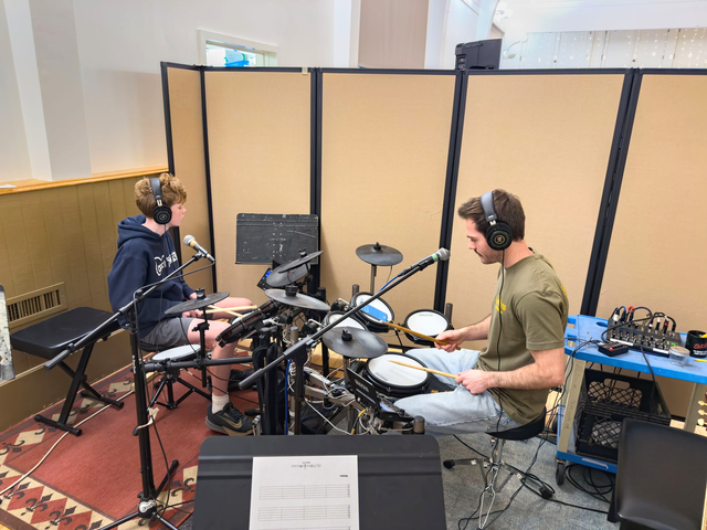 A boy and his teacher play the drums together during a music lesson.