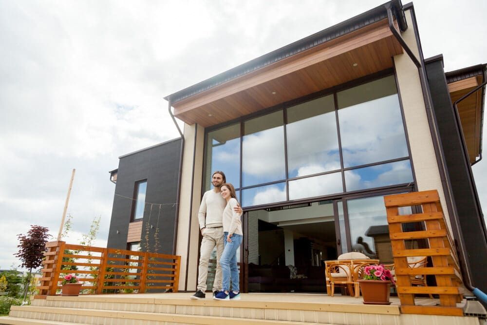 A Man And A Woman Are Standing In Front Of A Large House — Renovo Contractors In Monash, ACT
