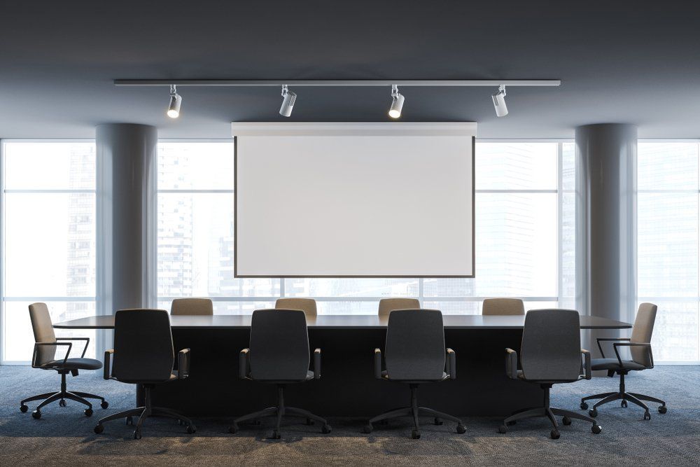 A Conference Room with A Long Table and Chairs and A Projector Screen — Renovo Contractors In Monash, ACT