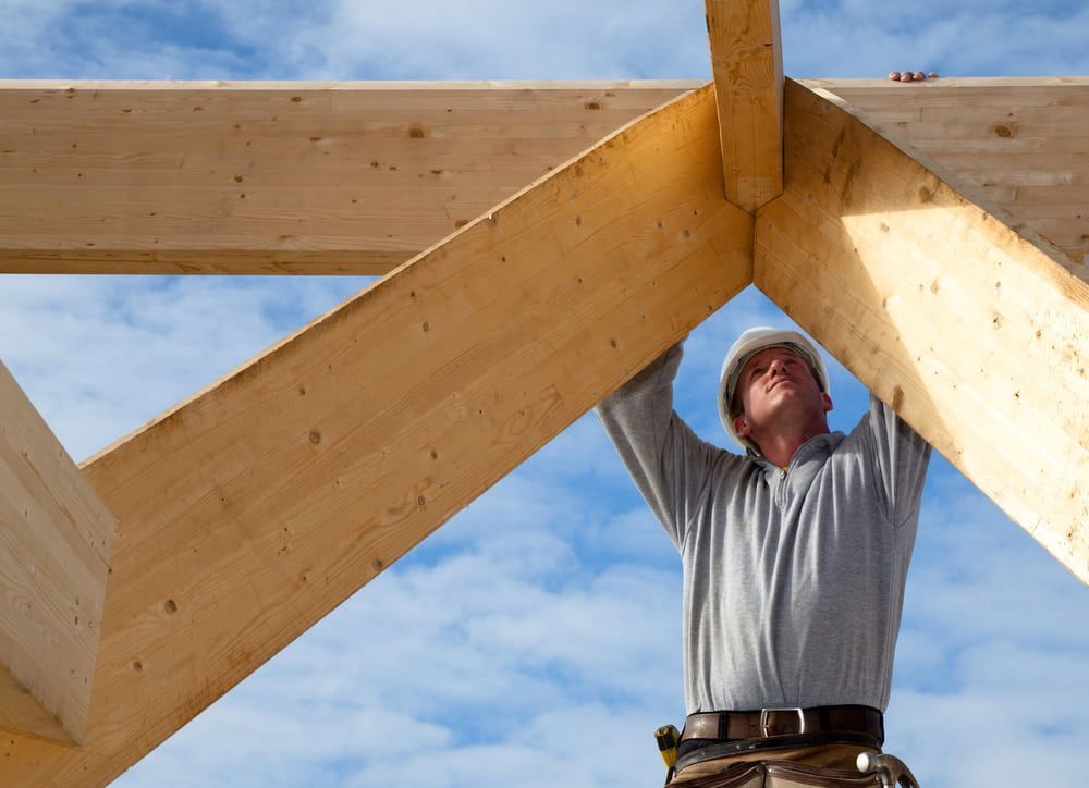 A Man Wearing A Hard Hat Is Working On A Wooden Structure — Renovo Contractors In Monash, ACT