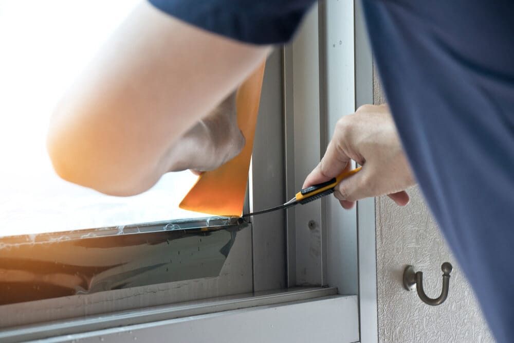 A Man Is Installing A Window With A Screwdriver — Renovo Contractors In Monash, ACT