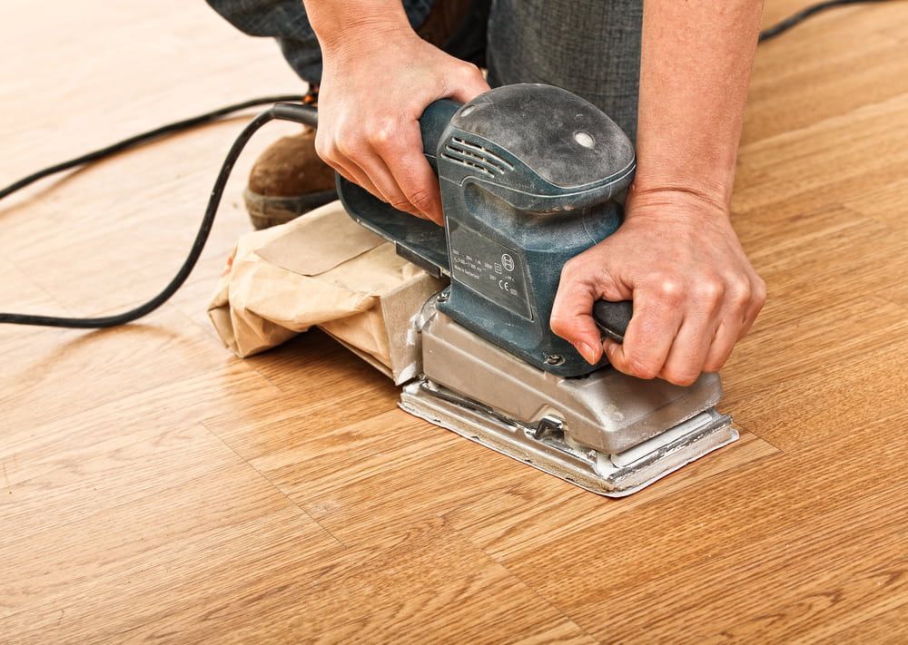 A Person Is Sanding A Wooden Floor With A Sander — Renovo Contractors In Monash, ACT