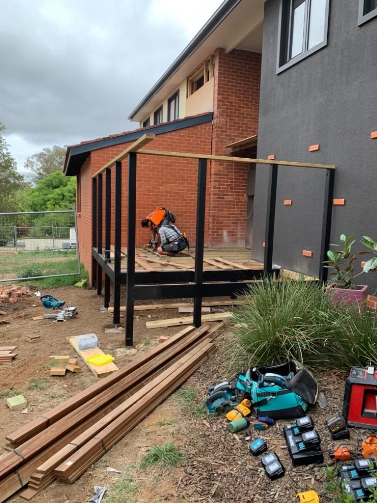 A man is working on a wooden deck in front of a house. — Renovo Contractors In Monash, ACT