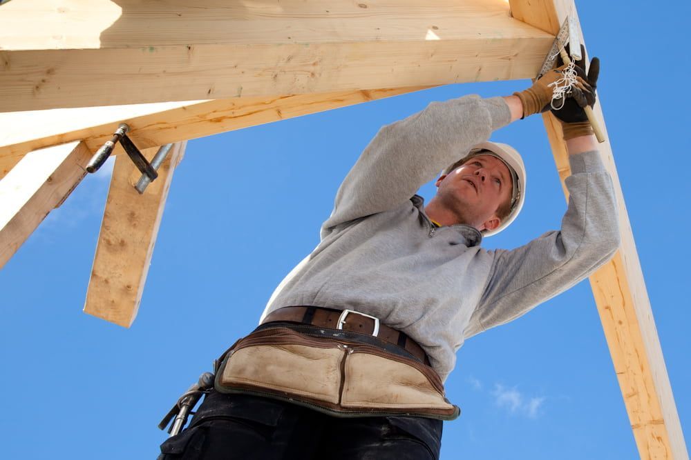 A Man Wearing A Hard Hat Is Working On A Wooden Structure — Renovo Contractors In Monash, ACT