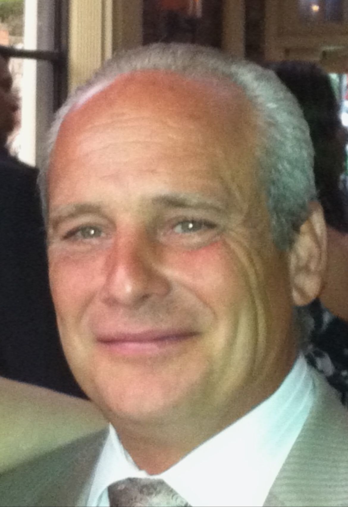 Close-up portrait of a smiling man in a light suit and white shirt at an indoor event