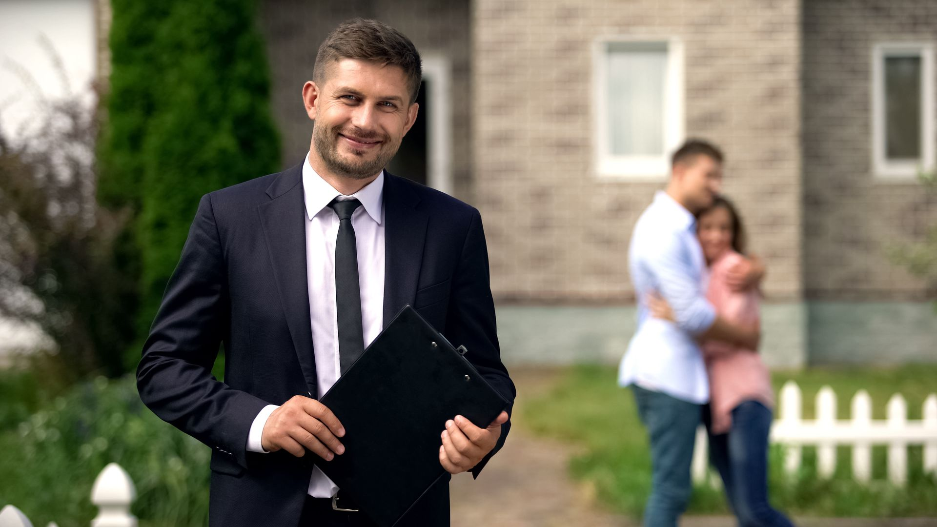 Real estate agent standing in front of a home after helping clients buy their new house.