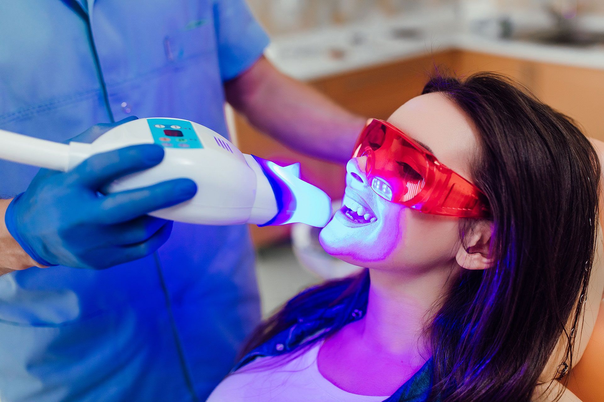 A woman is getting her teeth whitened by a dentist.