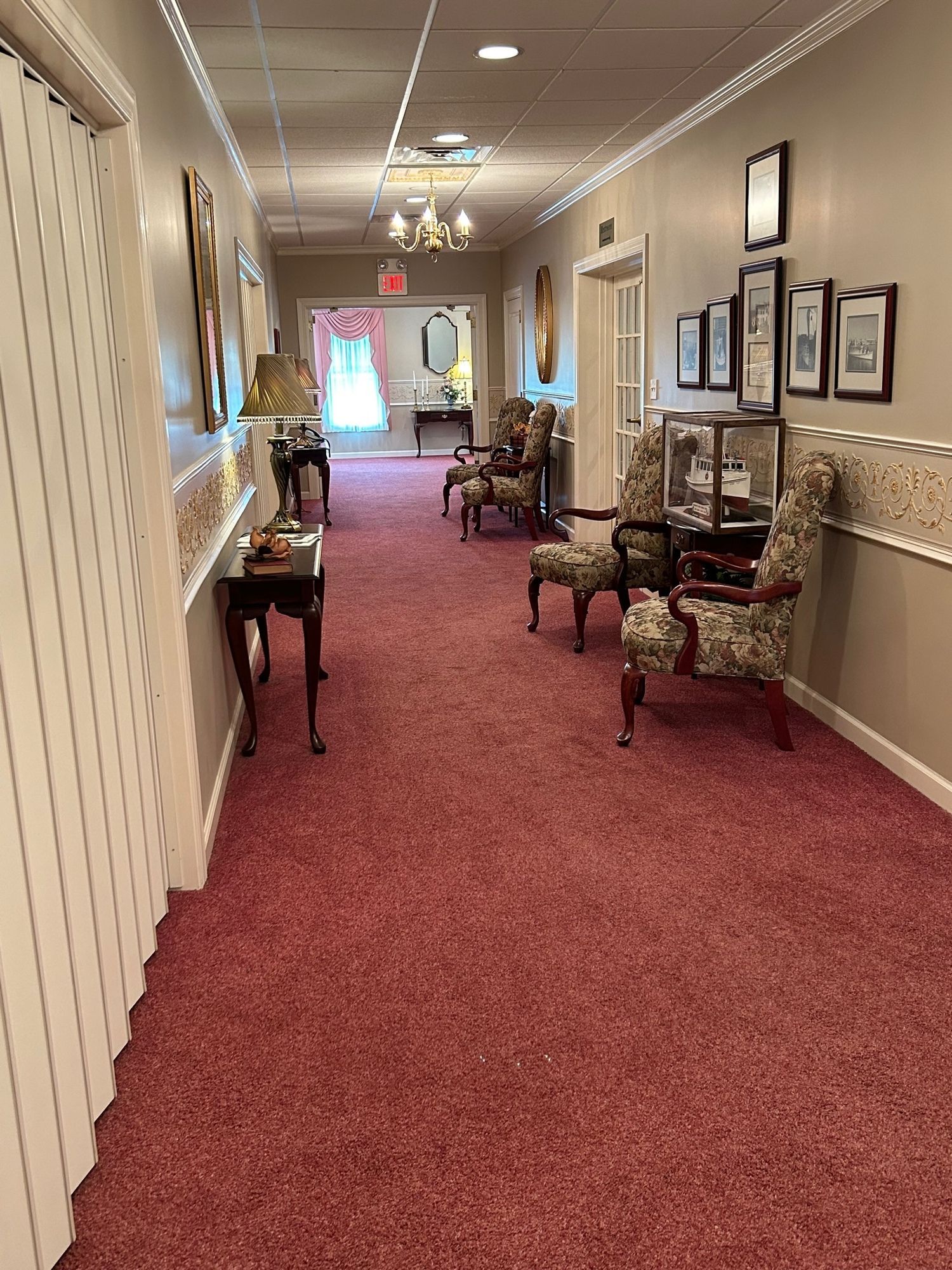 Long hallway with pink carpet, antique furniture, and framed artwork.