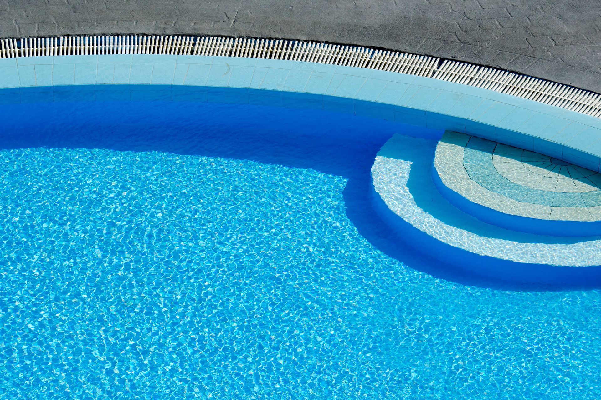 Blue swimming pool with curved steps and tiled edge