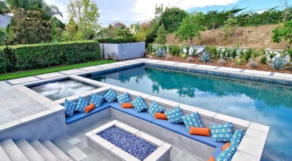 Modern backyard pool with spa, blue lounge cushions, and surrounding greenery