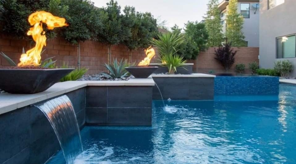 Modern backyard pool with waterfalls and fire bowls at dusk