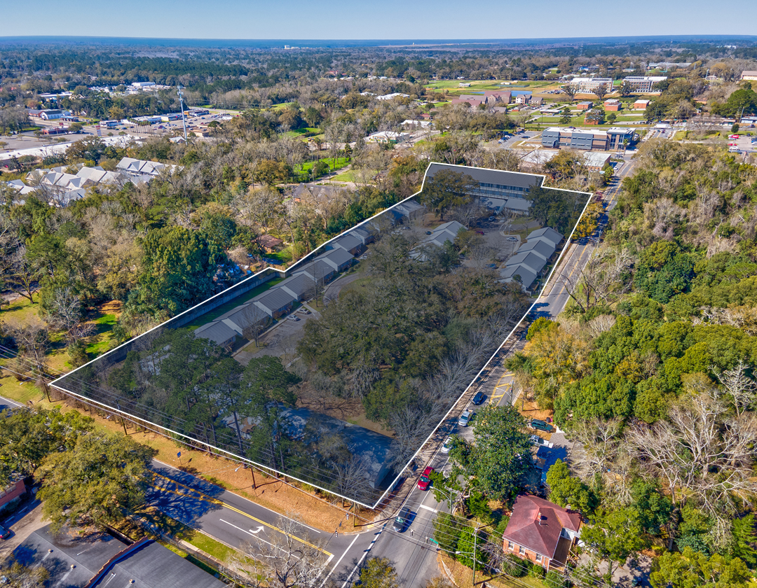 An aerial view of a large empty lot surrounded by trees and a road.