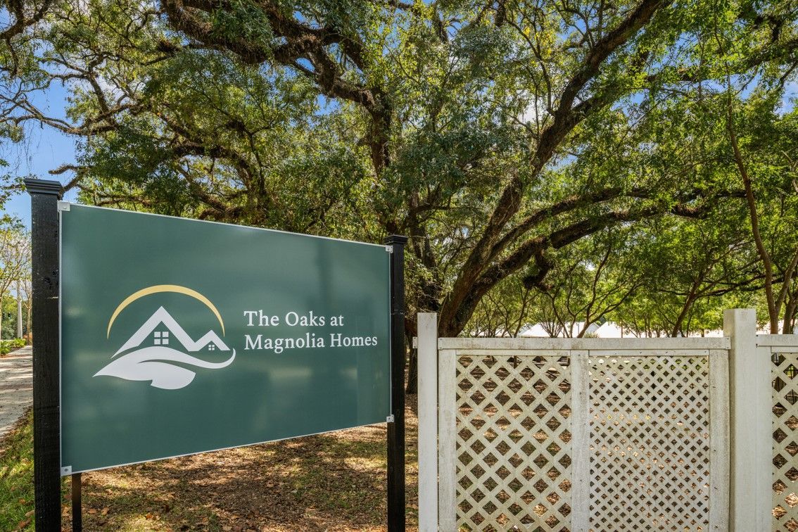 A sign for the oaks at magnolia home is sitting in front of a white fence.