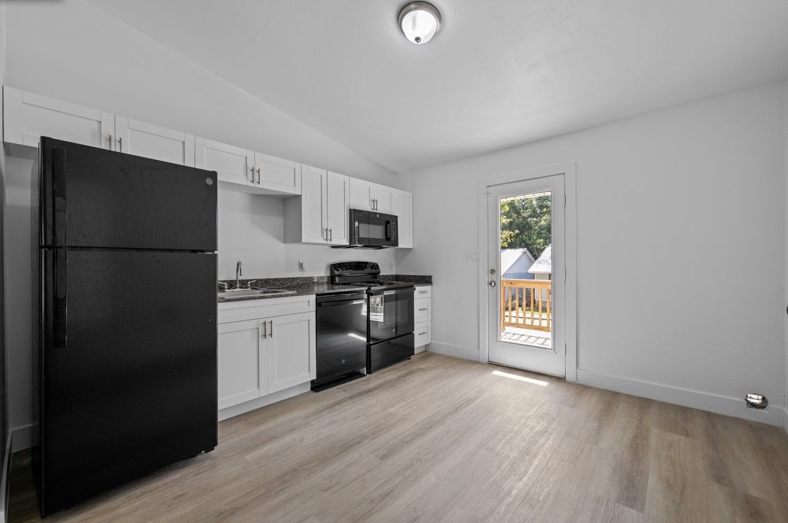 A kitchen with a black refrigerator , white cabinets , stainless steel appliances and hardwood floors.