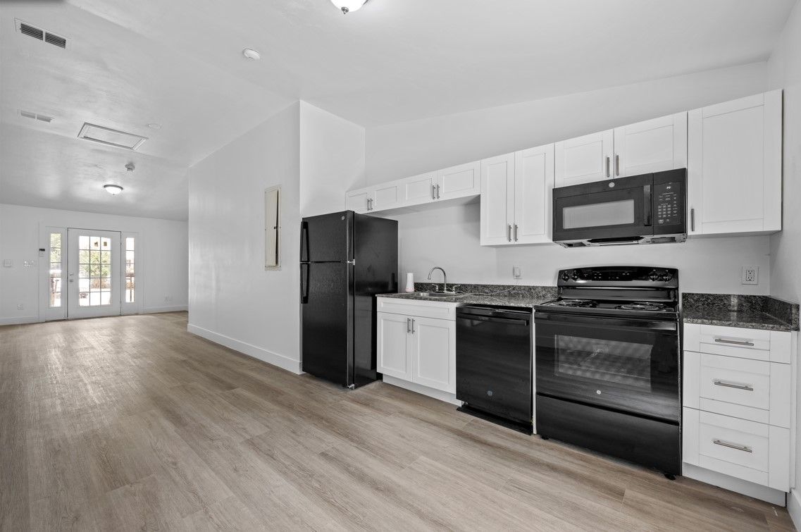 A kitchen with white cabinets , a black refrigerator , a black stove , and a microwave.