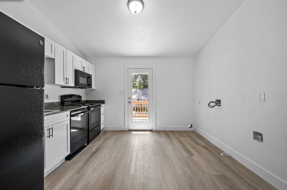 An empty kitchen with a black refrigerator and white cabinets.