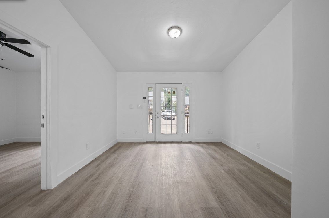 An empty living room with hardwood floors and white walls.