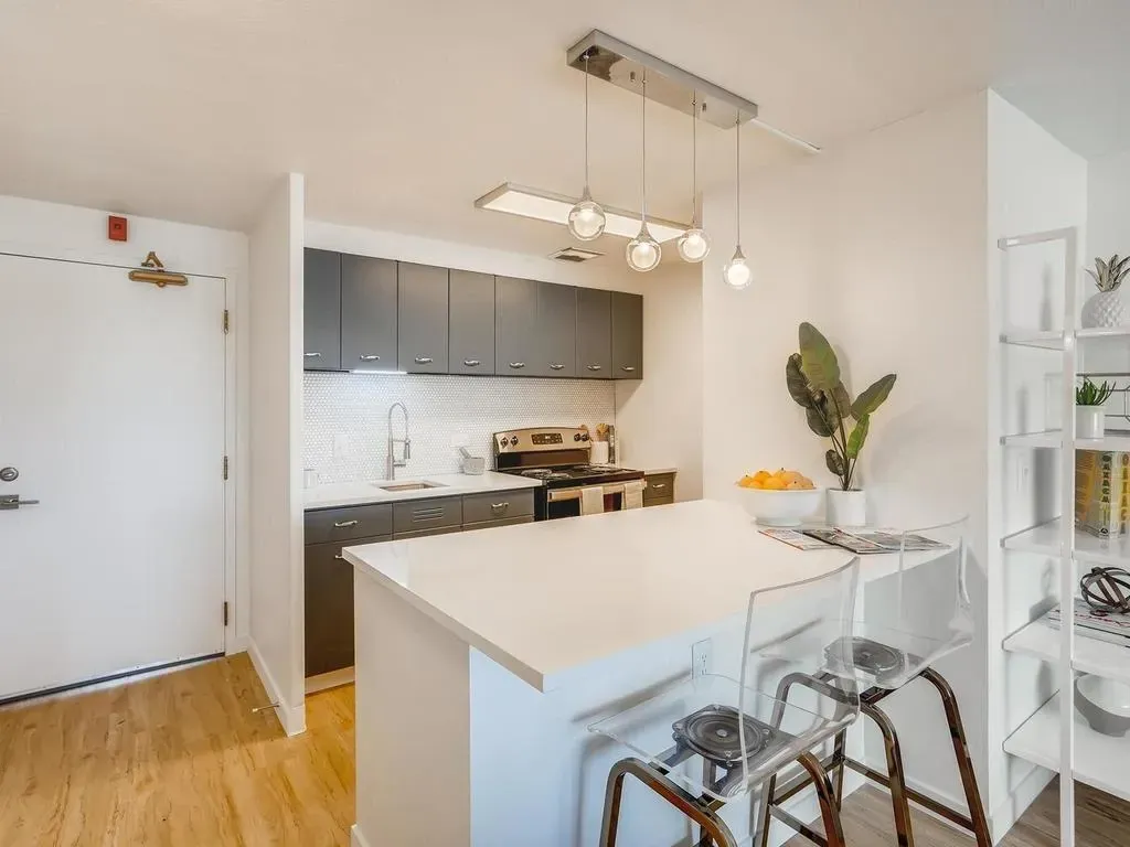Bright modern kitchen with white island, gray cabinets, pendant lights, and bar stools near the entryway