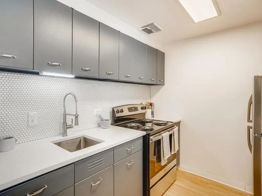 Modern kitchen with gray cabinets, white countertops, stainless stove, and tiled backsplash