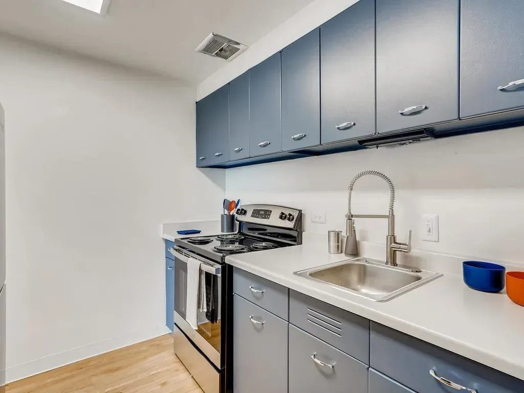 Modern kitchen with blue-gray cabinets, stainless steel stove, and sink on a white countertop