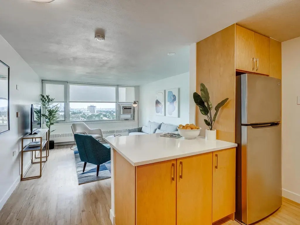 Bright open kitchen and living area with wood cabinets, white island, blue chairs, and large windows.