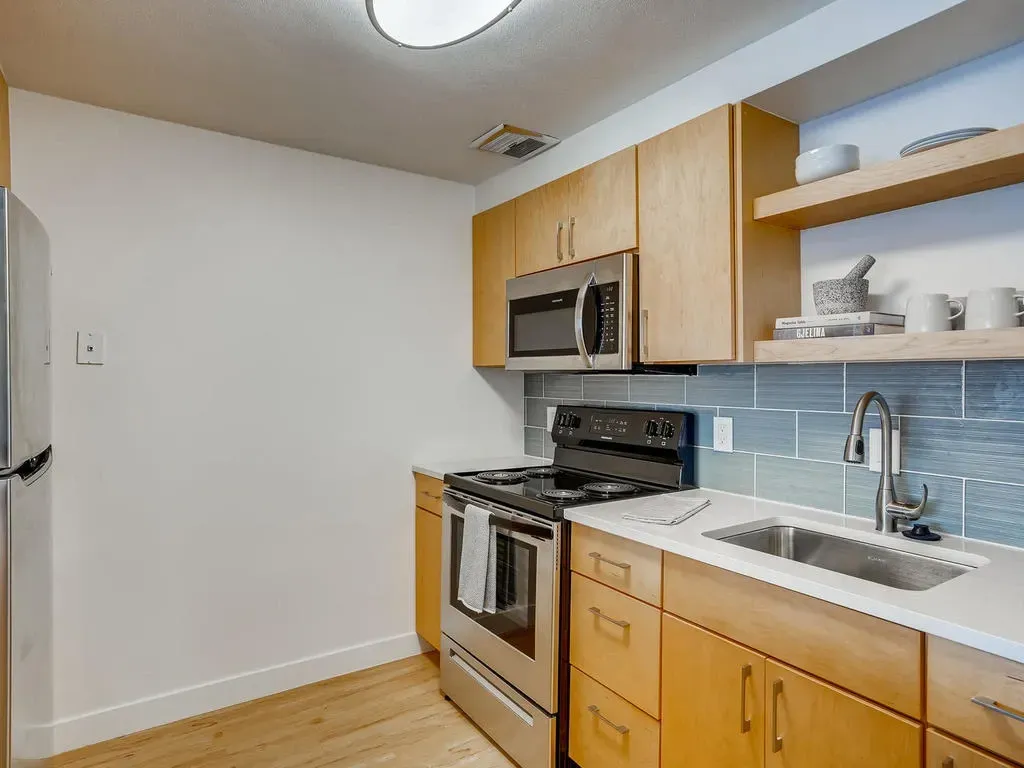Small modern kitchen with wooden cabinets, stainless stove, microwave, sink, and open shelves