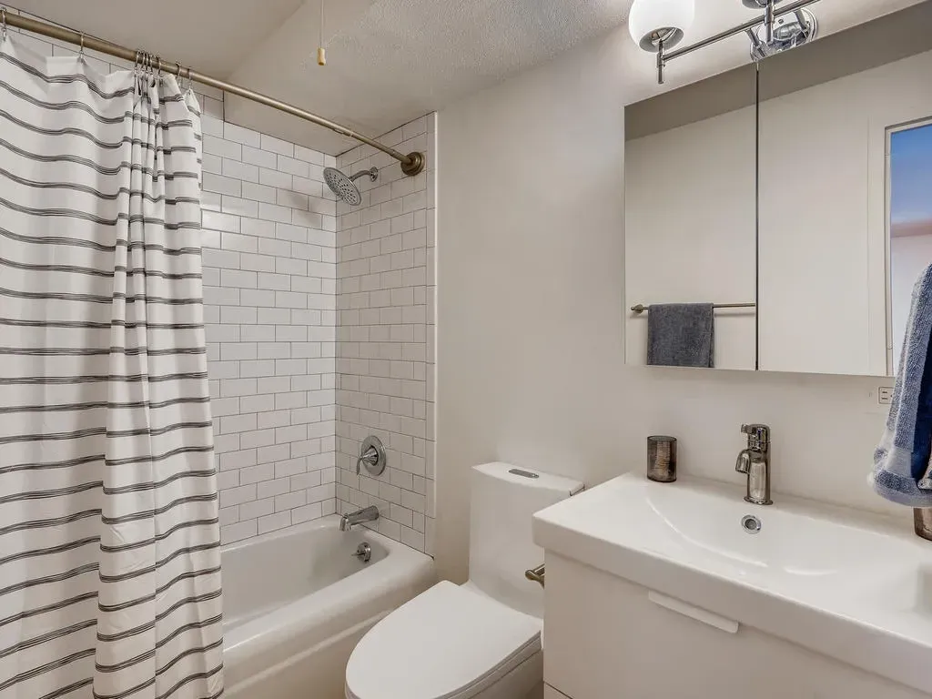Small bathroom with bathtub, shower curtain, white tile, and a sink with mirror cabinet
