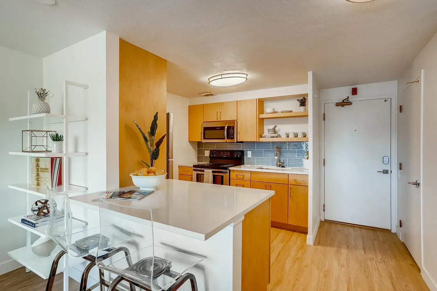Bright modern kitchen with wood cabinets, white island, dining nook, and entry door